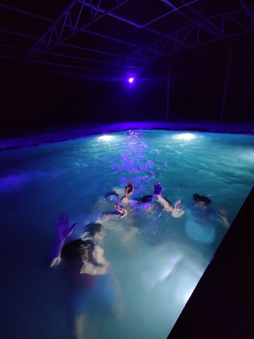 Guests enjoying a refreshing night swim in the illuminated blue pool under the stars