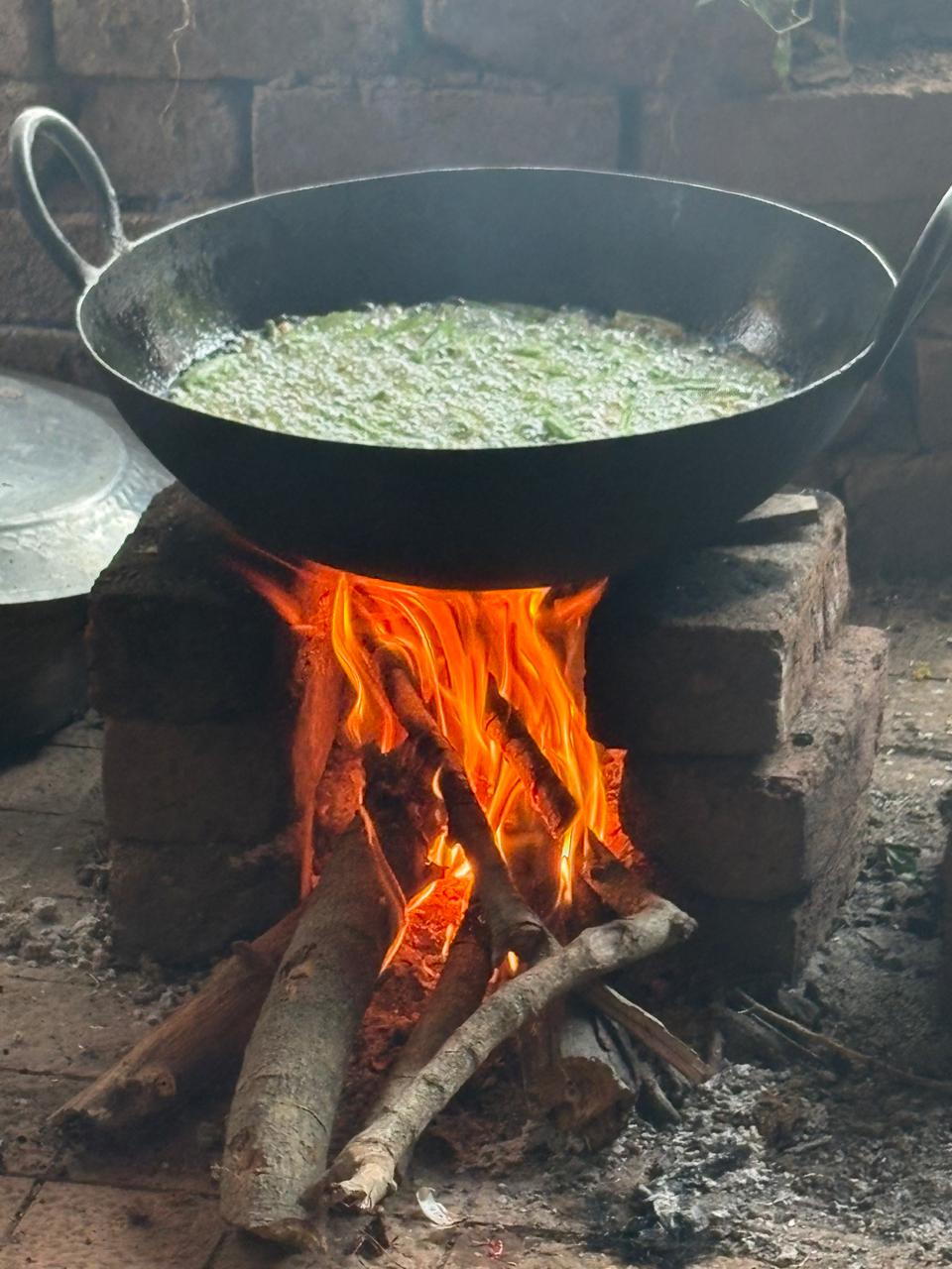 Flavorful green farm-fresh curry bubbling in a pot over an open wood fire